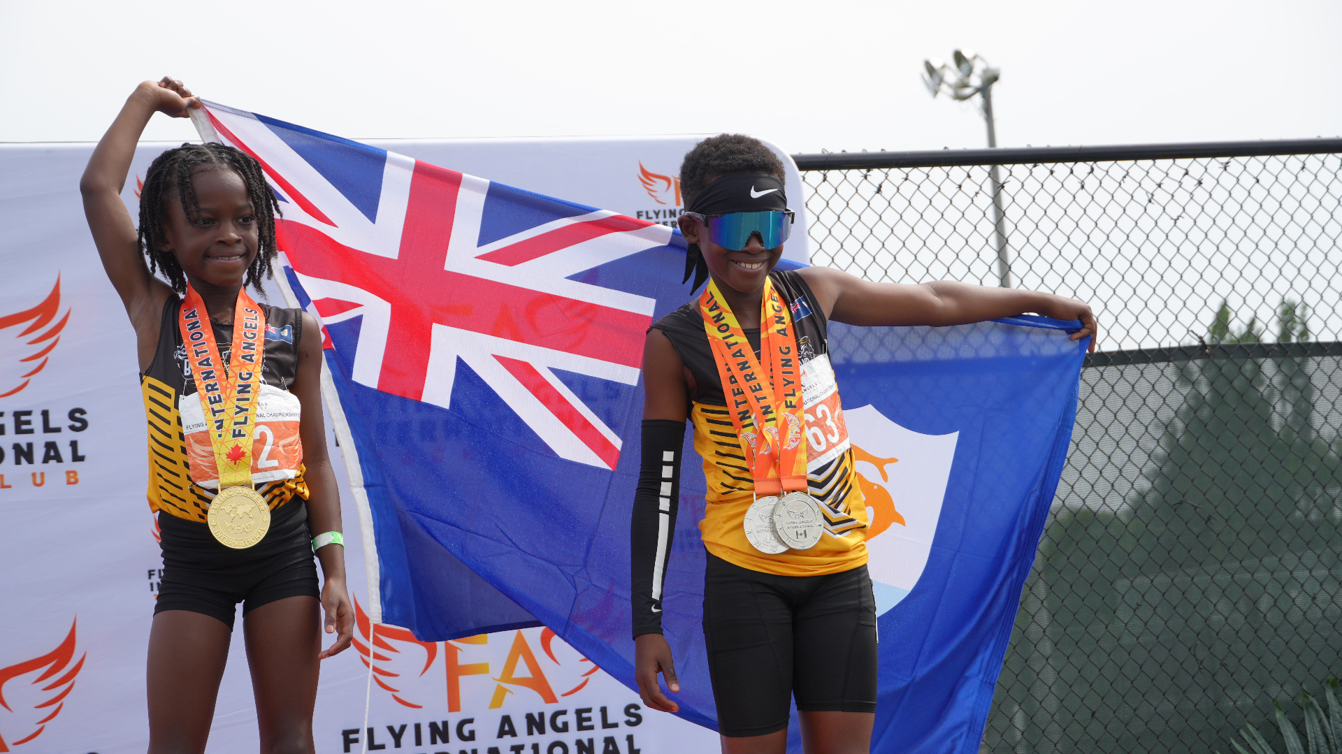 Two young athletes on the podium holding the Bermuda flag